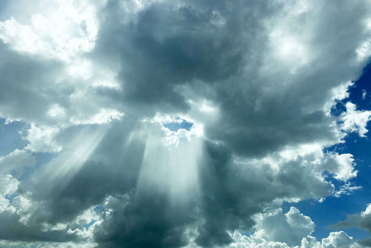 Captivating view of sunlight rays piercing through dark clouds in a vivid blue sky.