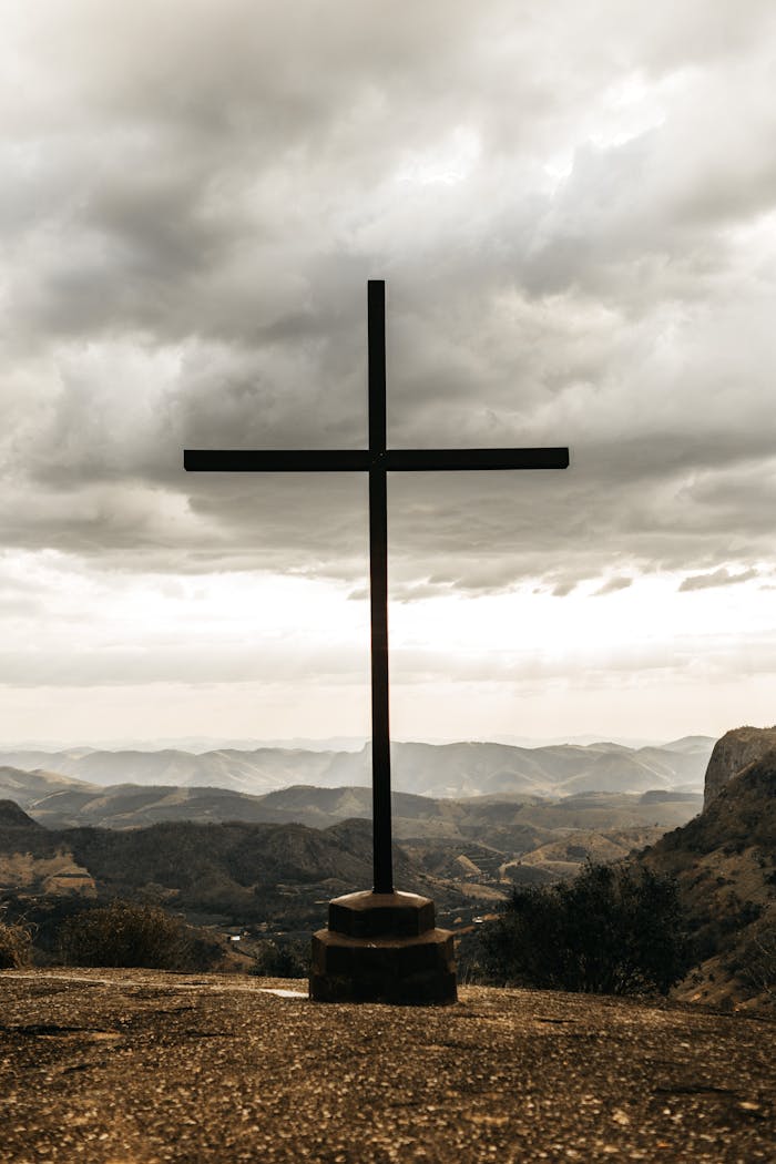 A powerful silhouette of a cross set against a dramatic cloudy mountain landscape.