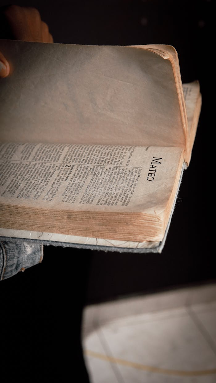 A close-up view of an open Bible, hand turning pages. Focus on the book of Matthew.
