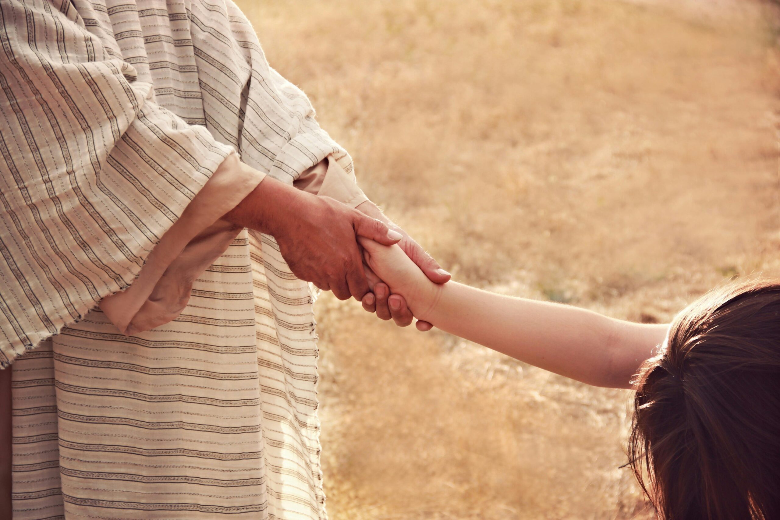 A close-up of a person in traditional clothing shaking hands with a child outdoors.