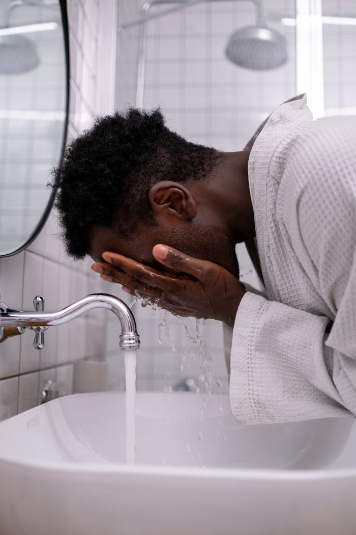A man in a bathrobe washes his face in a modern bathroom sink.